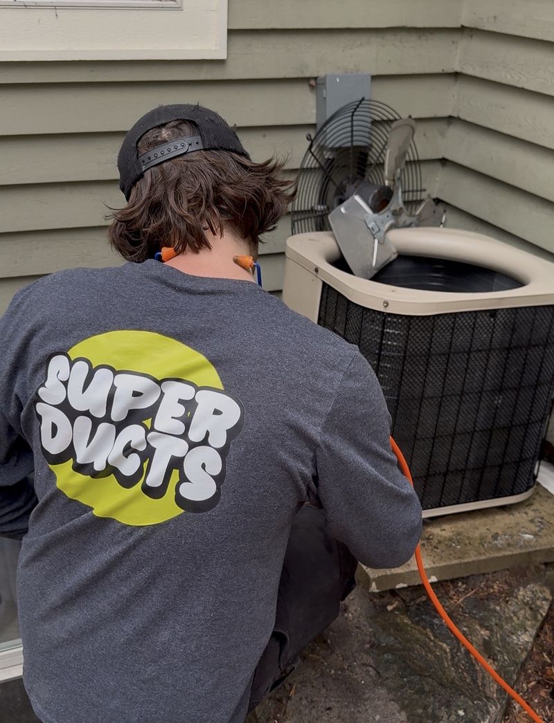 Super Ducts technician cleaning an outdoor A/C condenser with the fan lifted out